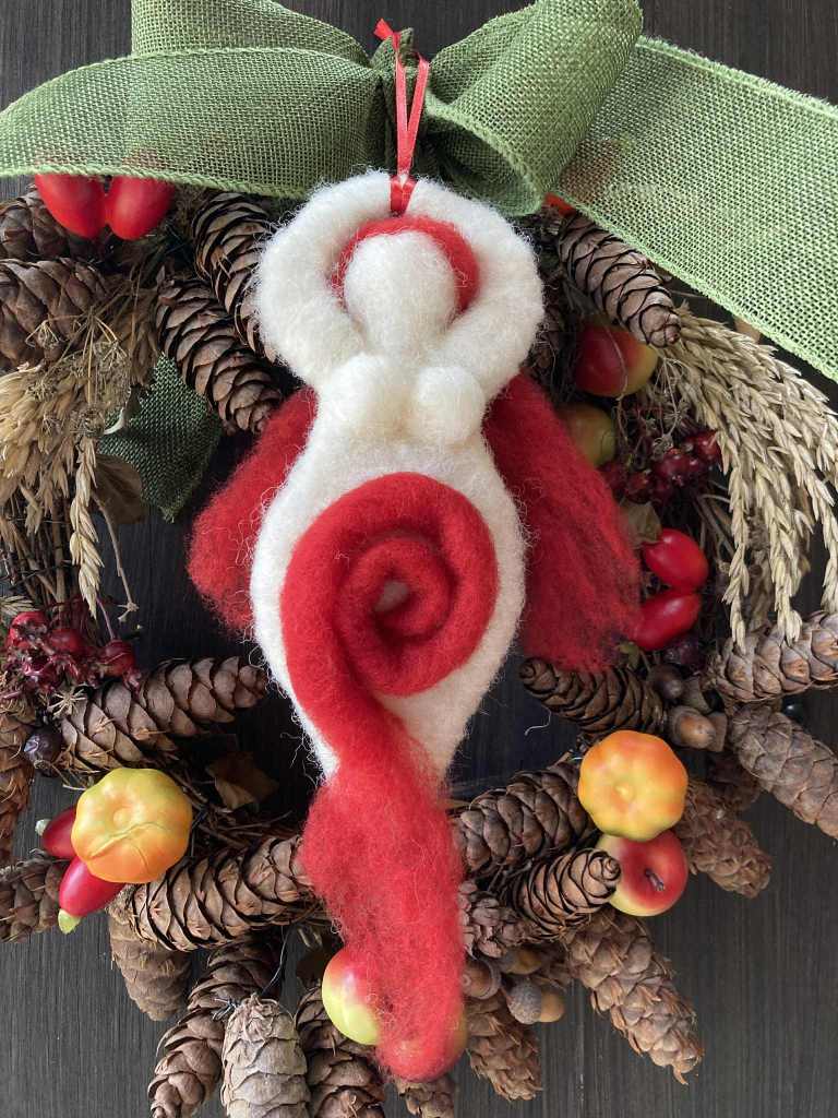 A felt goddess figure in front of a Yule wreath